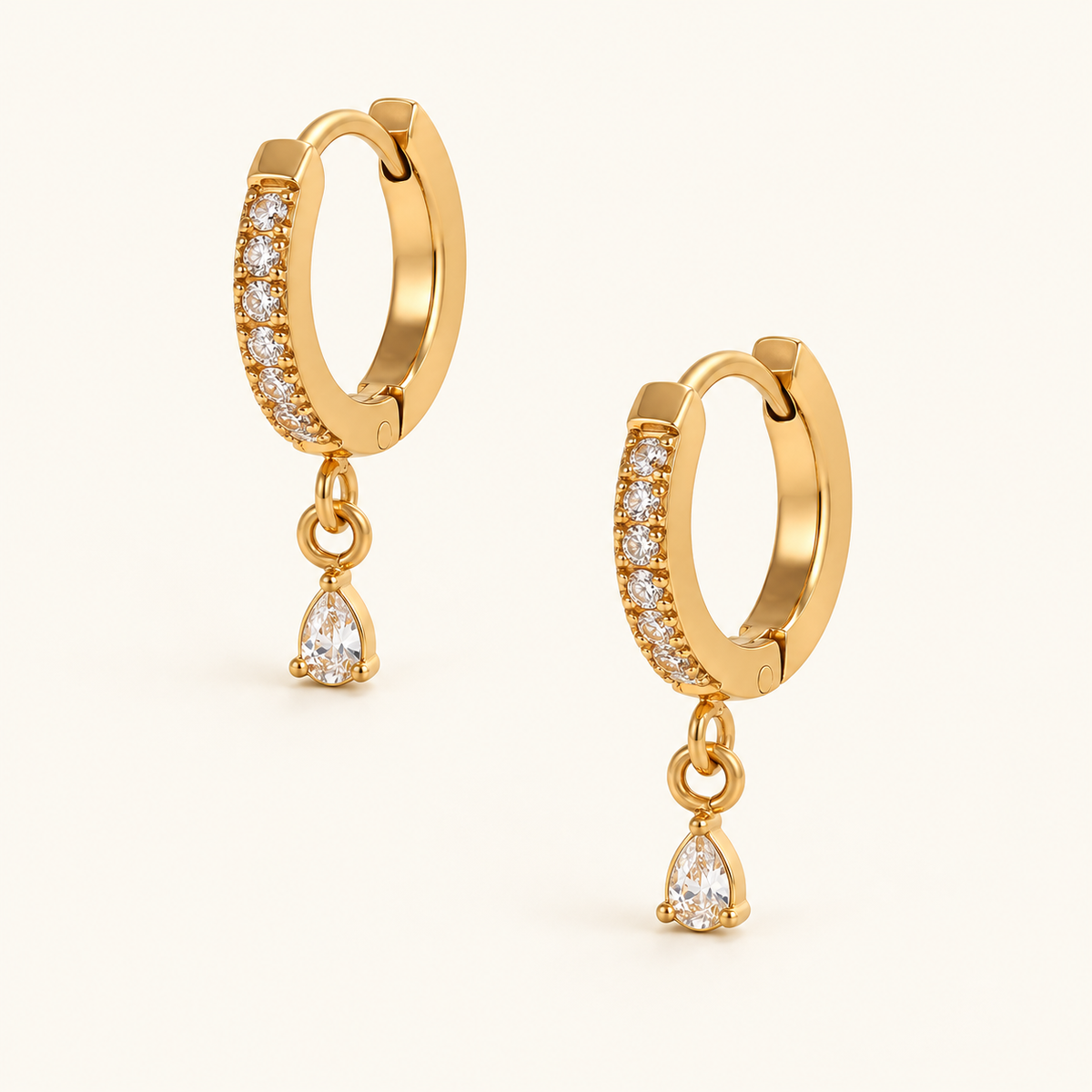 Nia Pear Hoops with crystal-lined gold-tone hoops and single pear-shaped clear drops on an ivory background